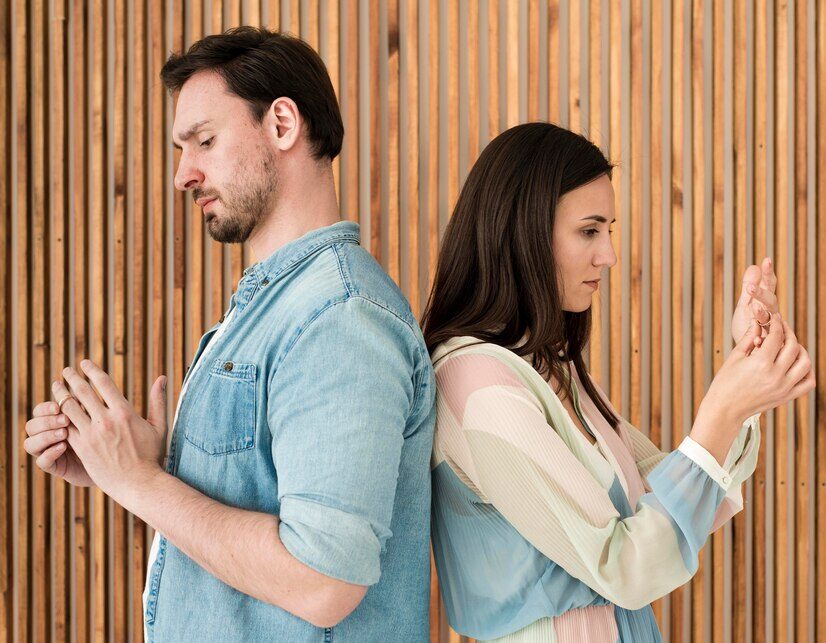 Couple éloigné, dos à dos, touchant leurs bagues de mariage, symbolisant une rupture émotionnelle dans une relation.
