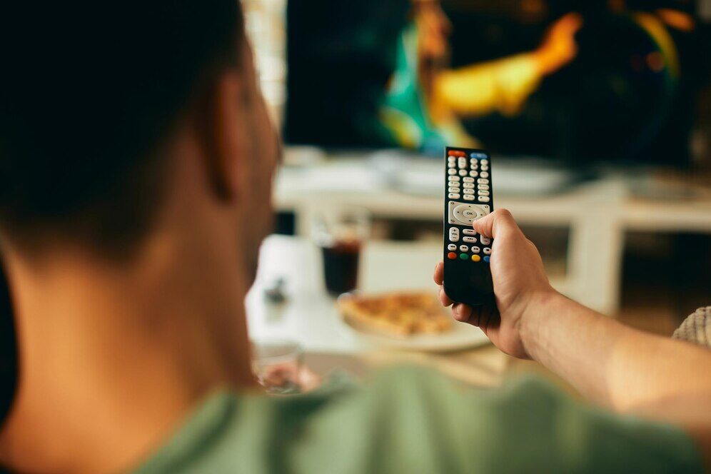 Homme sur son canapé regardant une publicité TV, symbolisant l'influence des médias sur les comportements et les relations.